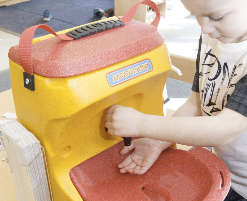 Preschool boy washing hands with KiddiWash portable handwash unit