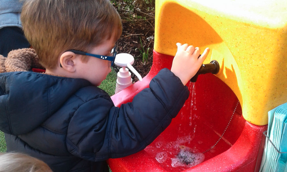 Child washing his hands outside with a KiddiSynk portable sink